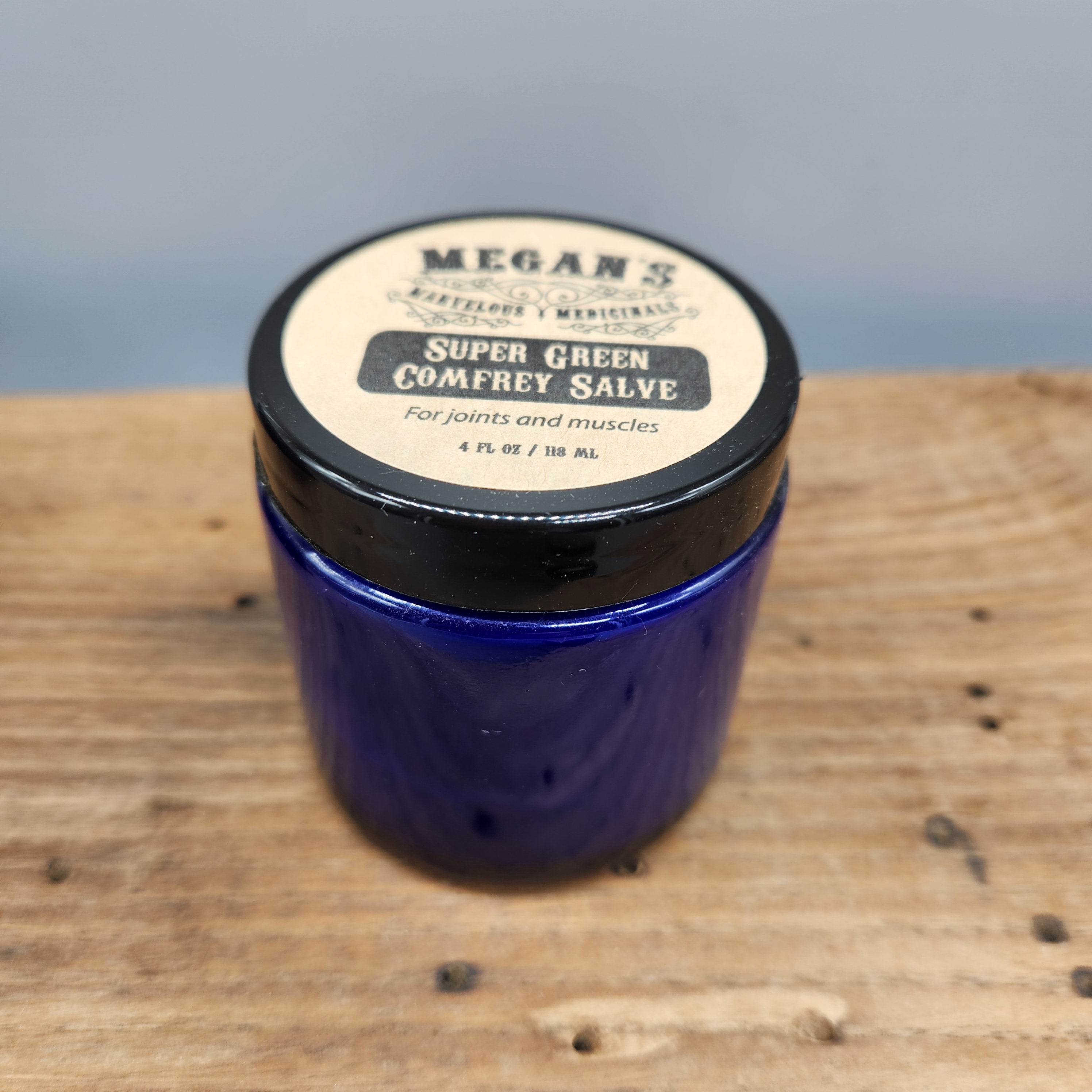 Blue jar of Megan's Marvelous Medicinals 4 oz super green comfrey salve on a wooden surface