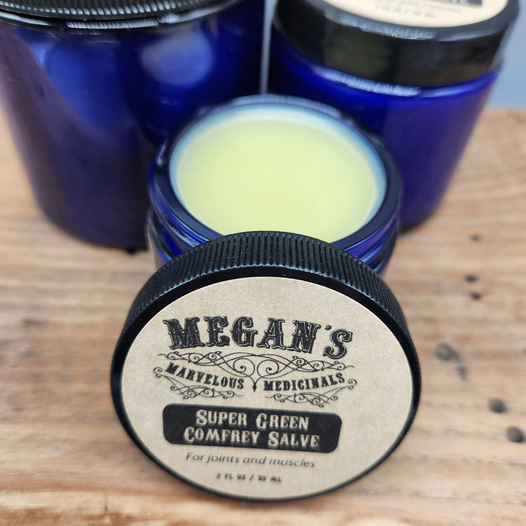 Balm container with Megan's Marvelous Medicinals branding on a wooden surface. showing super green comfrey salve